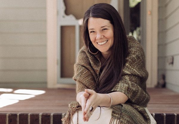 Jessica Flowers, founder and certified clinical herbalist, smiling on a porch wrapped in a woven shawl