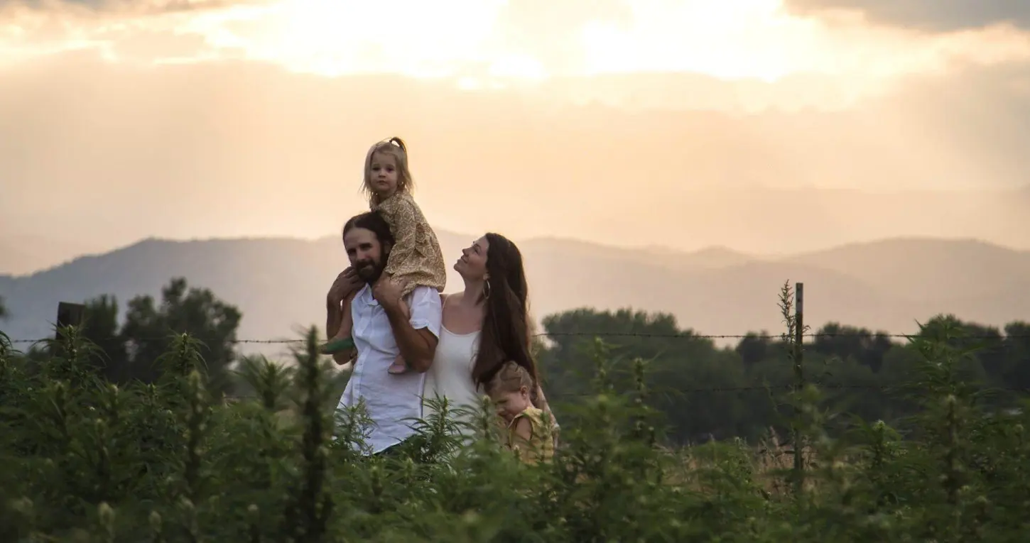 Edward, Jessica and their daughters in a hemp field at sunset, with the Colorado foothills behind them