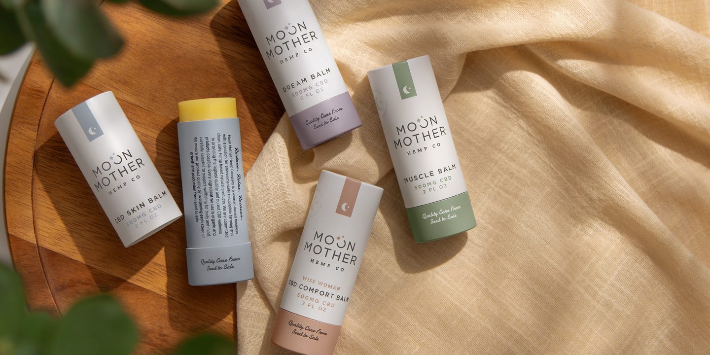 Five CBD balm sticks on a wooden tray with linen and eucalyptus