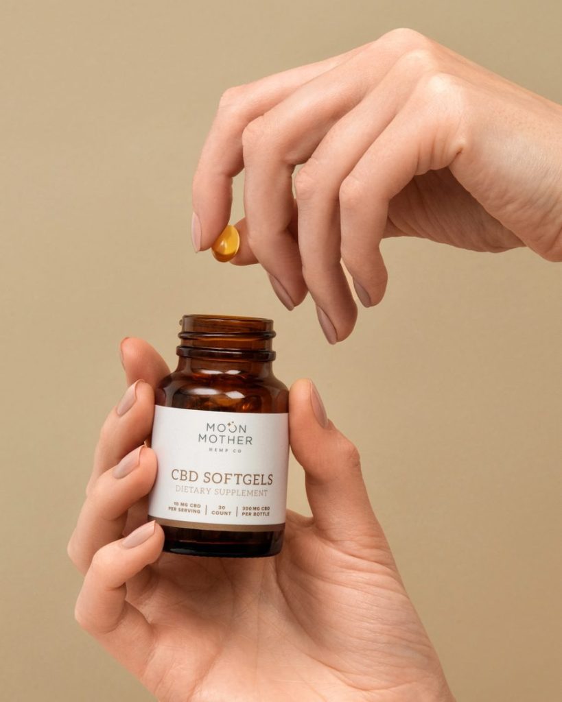 Hand dropping a softgel into its amber bottle