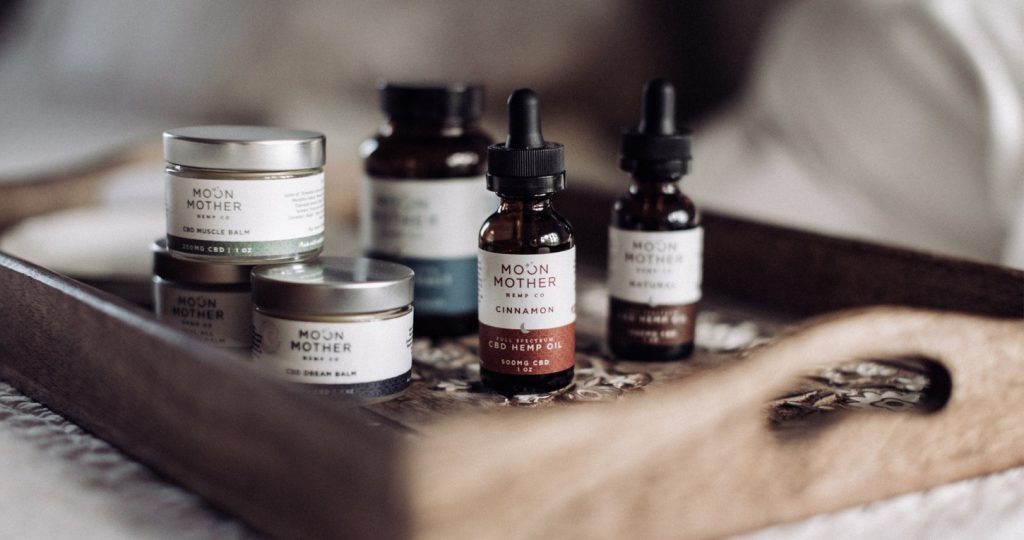 Moon Mother balms and hemp oil tinctures on a wooden tray